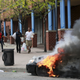 People with goods looted from a store walk near burning vehicles.